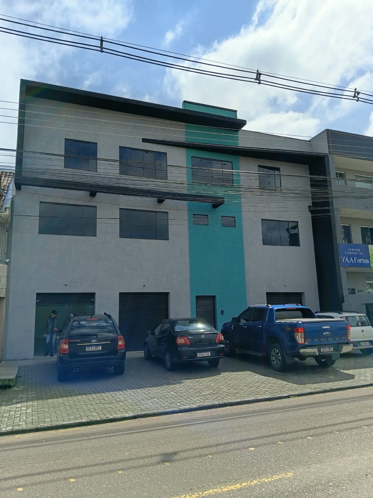 Fachada de prédio comercial em cinza, com faixa verde e detalhes escuros.