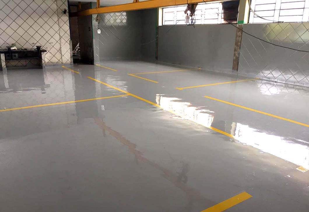 Piso cinza pintado com demarcações amarelas em ambiente de trabalho.